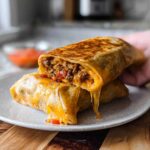 A close-up of a Grilled Cheese Burrito cut in half, showing a gooey, melted cheese pull and savory filling.