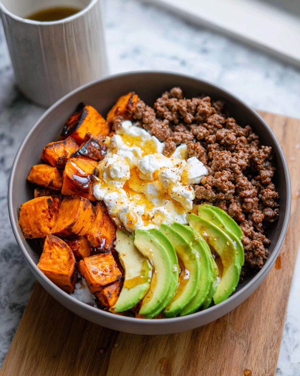A delicious Ground Beef Hot Honey Bowl featuring seasoned ground beef, roasted sweet potatoes, creamy cheese, sliced avocado, and a drizzle of honey.
