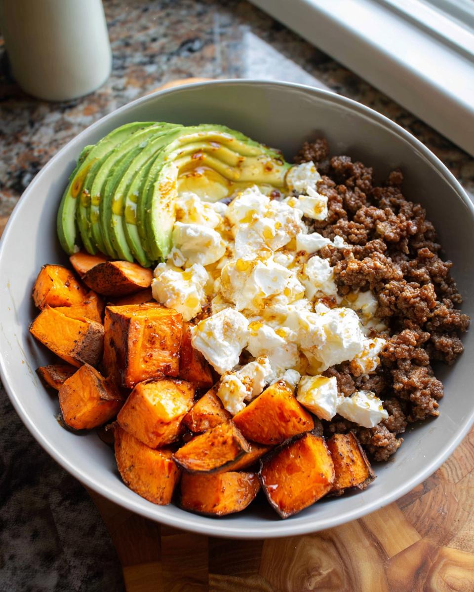 A close-up of a Ground Beef Hot Honey Bowl featuring seasoned ground beef, crumbled cheese, sliced avocado, and roasted sweet potato cubes.