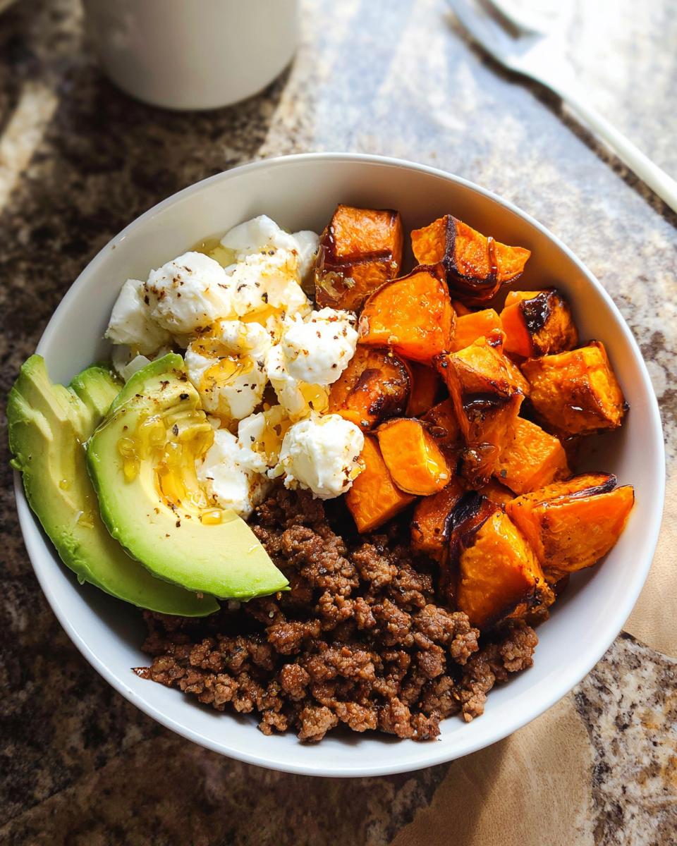 A close-up of a Ground Beef Hot Honey Bowl featuring seasoned ground beef, roasted sweet potatoes, crumbled cheese, and avocado slices.