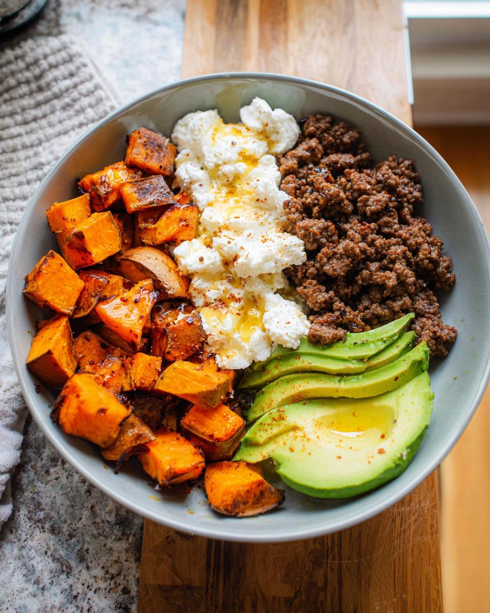 A delicious Ground Beef Hot Honey Bowl featuring roasted sweet potatoes, crumbled cheese, seasoned ground beef, and sliced avocado.