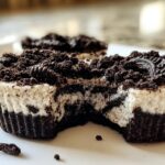 A close-up of a healthy no-bake Oreo cheesecake bite with a bite taken out, showing the creamy filling and cookie crust.
