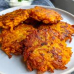 A plate of golden-brown, crispy Healthy Sweet Potato Hash Browns, with a small bowl of dip in the background.