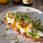 A high-protein breakfast wrap featuring cottage cheese, avocado, and a perfectly poached egg on toasted bread, topped with sprouts.