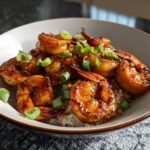 A close-up of a bowl filled with fluffy white rice topped with glistening High-Protein Honey Garlic Shrimp and chopped green onions.