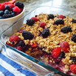 A freshly baked High Protein Triple Berry Bake in a glass dish, topped with whole berries and a crumble topping.