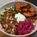 A delicious Hot Honey Chicken Bowl featuring sliced chicken, roasted sweet potatoes, rice, pickled onions, and a creamy sauce.