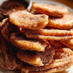 A close-up of a stack of Irresistible Spanish Churro Pancakes, coated in cinnamon sugar, with a small bowl of chocolate dip in the background.