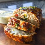 A close-up of a slice of Juicy Garlic Parmesan Chicken Meatloaf, showing melted cheese and a glaze.