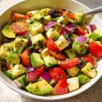 A bowl of Simple & Zesty Mediterranean Avocado Egg Salad with diced avocado, tomatoes, olives, red onion, and feta cheese.