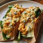 Two Spicy Buffalo Chicken Wraps filled with shredded chicken, spinach, blue cheese, and drizzled with sauce.