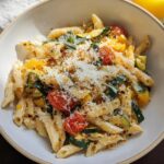 A bowl of delicious Tomato Zucchini Pasta topped with grated Parmesan cheese and fresh herbs.