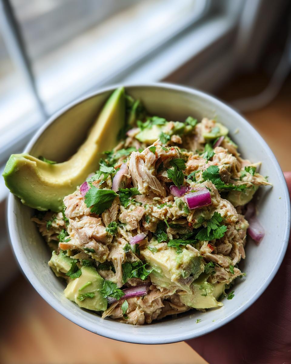 A bowl of creamy avocado tuna salad with chunks of avocado, red onion, and cilantro. Healthy lunch ideas.