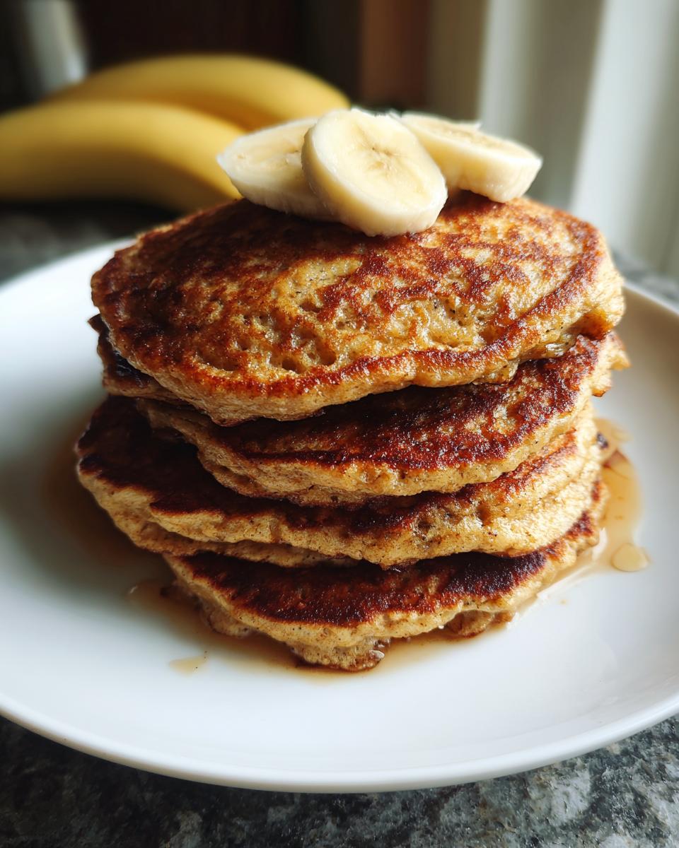 A stack of fluffy banana oat pancakes topped with sliced bananas and drizzled with syrup.