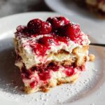 A slice of Cherry Amaretto Tiramisu on a white plate, topped with fresh cherries and powdered sugar.