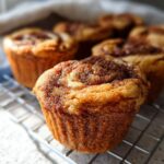 Close-up of freshly baked Cinnamon Roll Protein Muffins on a cooling rack, showing swirled cinnamon topping.