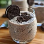 A glass of creamy Cookies and Cream Mousse topped with crushed Oreos and a whole Oreo cookie.