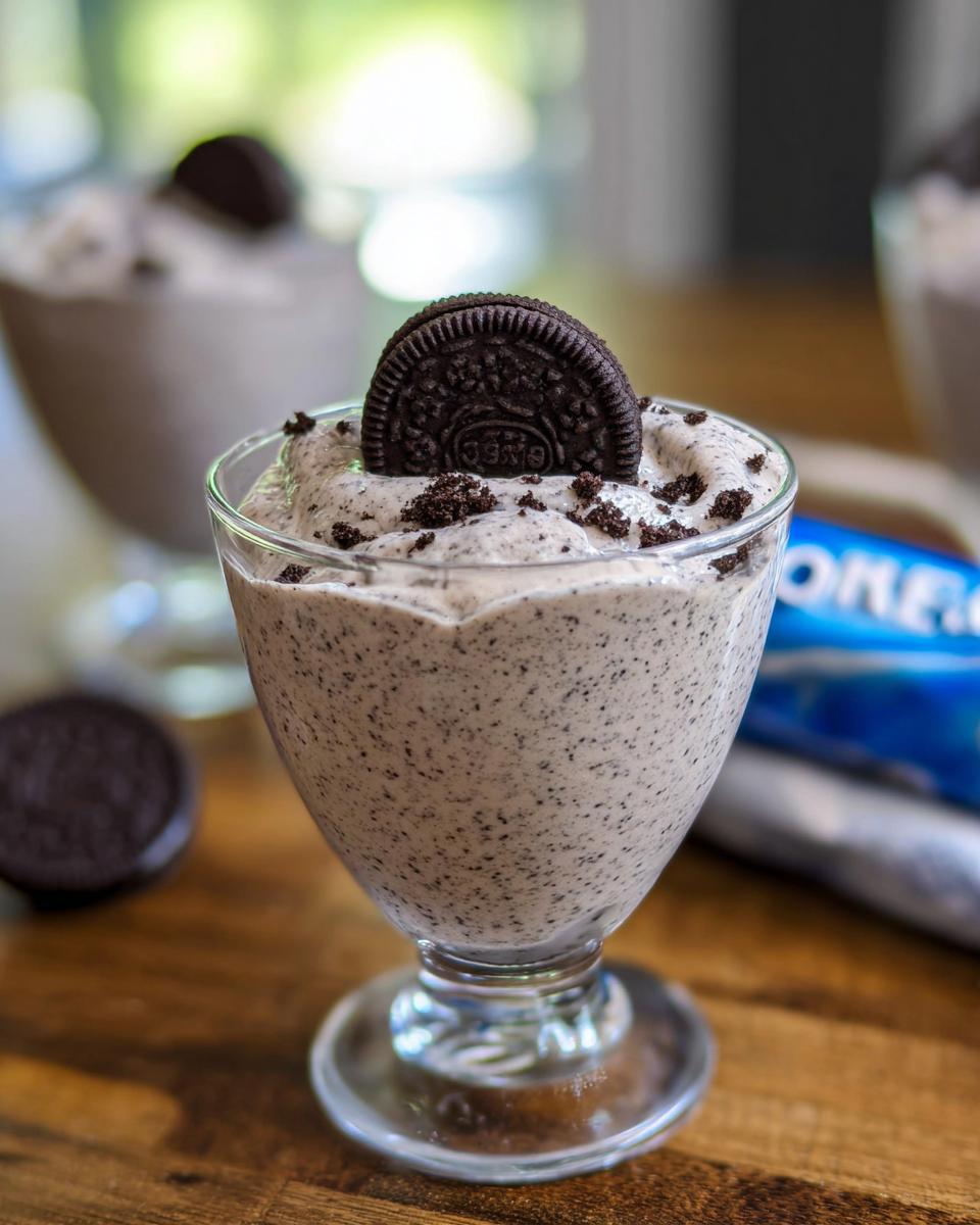 A close-up of a glass filled with creamy Cookies and Cream Mousse, topped with an Oreo cookie and cookie crumbs.
