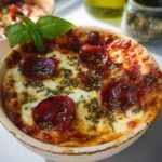 A close-up of a bubbling Cottage Cheese Pizza Bowl topped with melted cheese, pepperoni, and herbs, garnished with fresh basil.