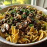 A bowl of creamy beef stroganoff with mushrooms and noodles, garnished with parsley. A delicious ground beef recipe.