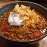 A hearty bowl of creamy taco soup topped with sour cream, shredded cheese, and tortilla chips.