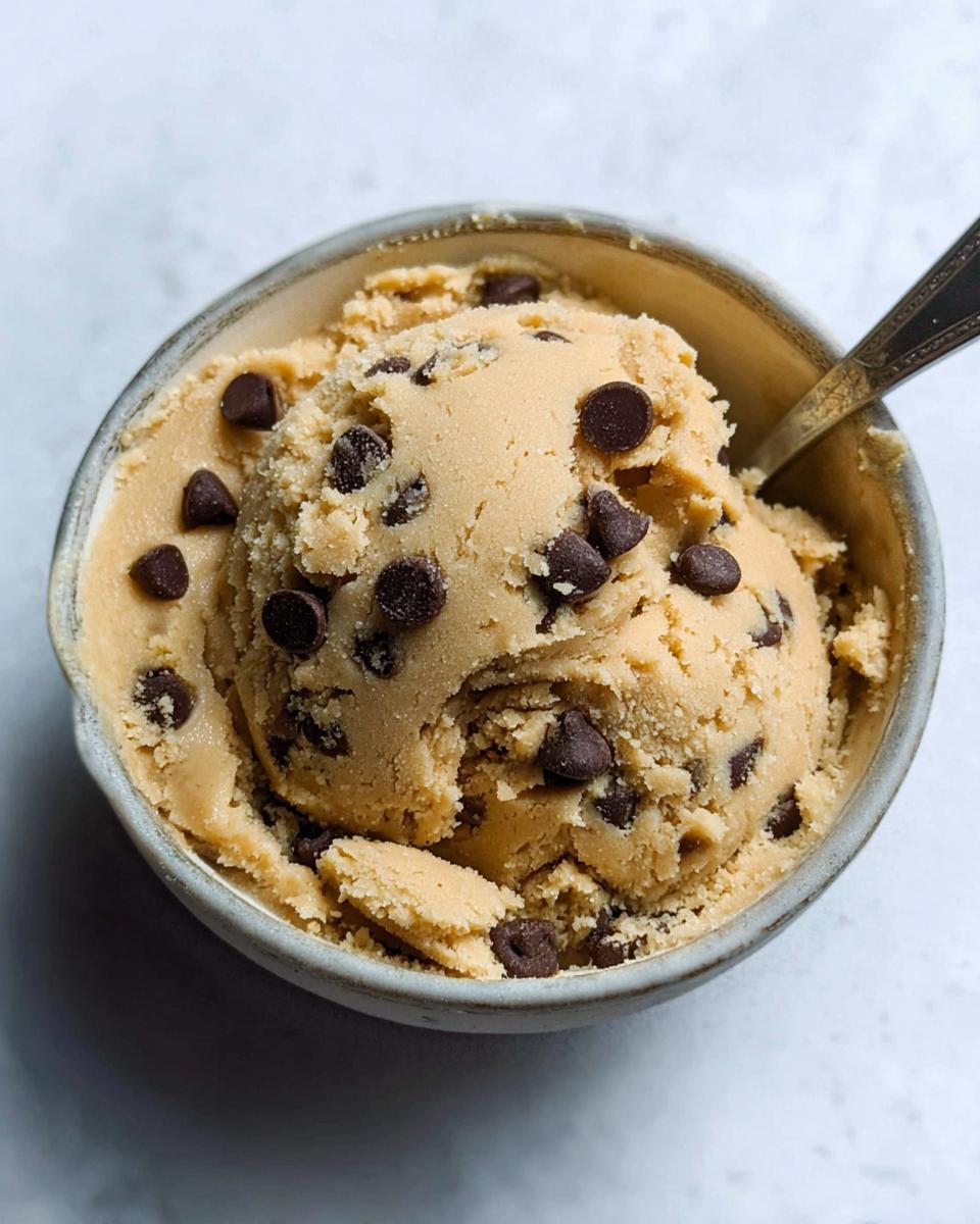 A bowl of delicious protein cookie dough loaded with chocolate chips, with a spoon taking a bite.