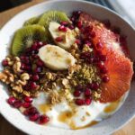 A vibrant and healthy Easy Yogurt Granola Bowl topped with kiwi, banana, pomegranate, blood orange, walnuts, and honey.