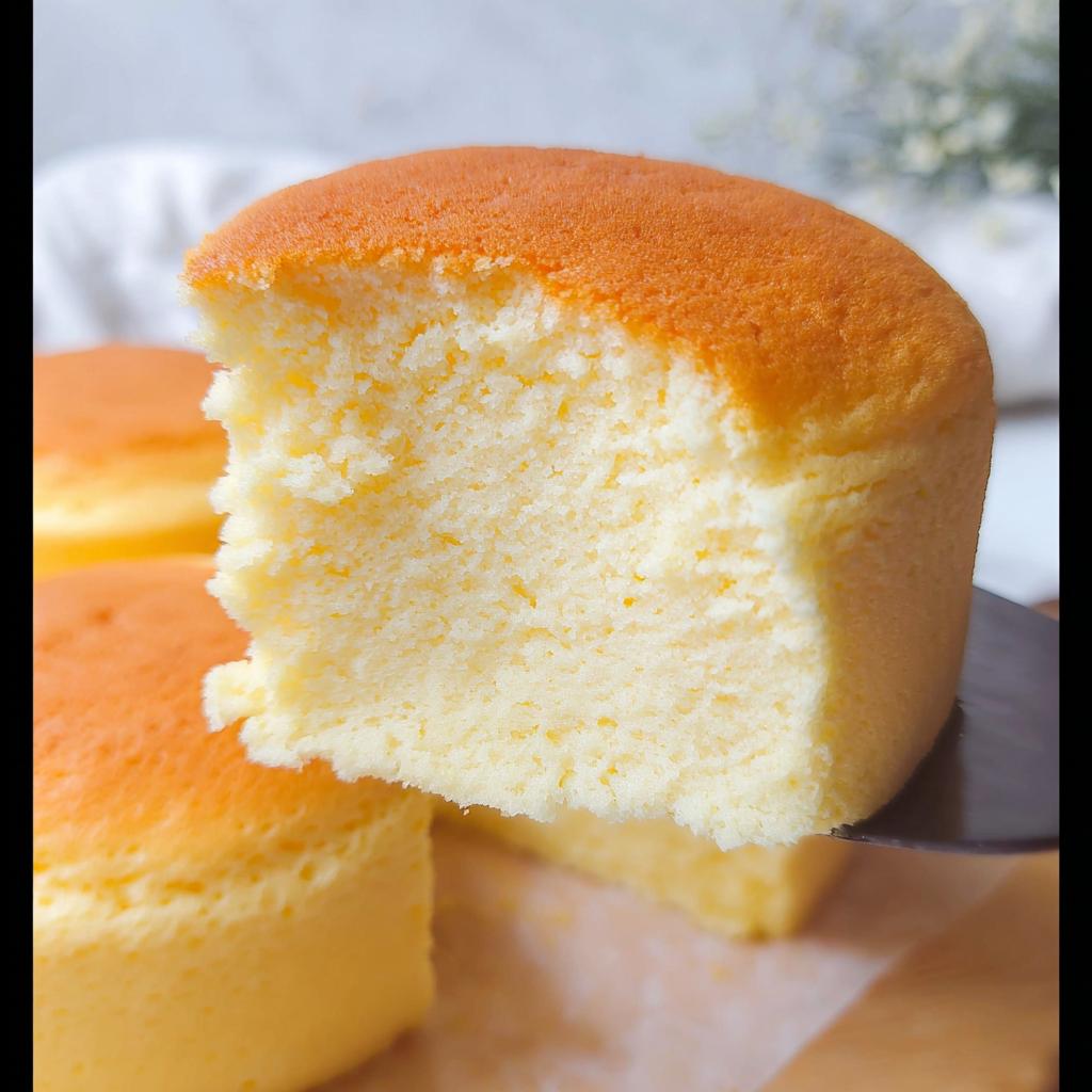 A slice of fluffy Japanese cotton cheesecake cupcake being lifted, showing its airy texture and golden-brown top.