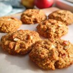 A close-up of several freshly baked Gesunde Apfel-Hafer-Kekse (healthy apple oat cookies) with visible apple chunks and oats.