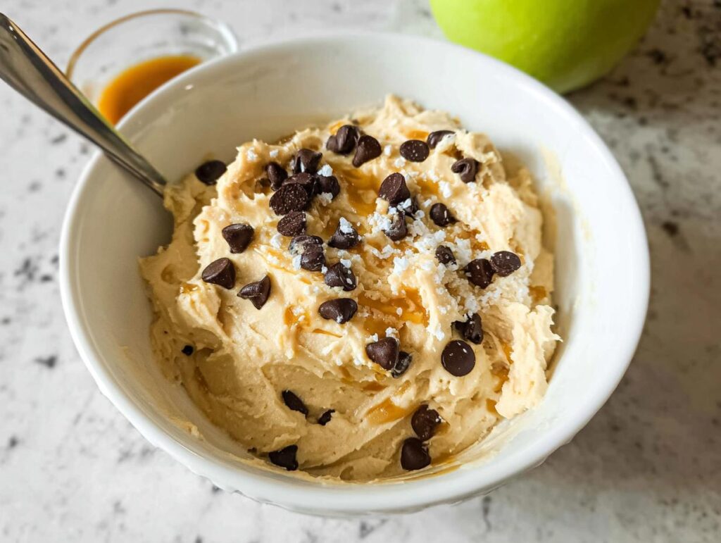 A bowl of Greek Yogurt Cookie Dough topped with chocolate chips and a caramel drizzle.