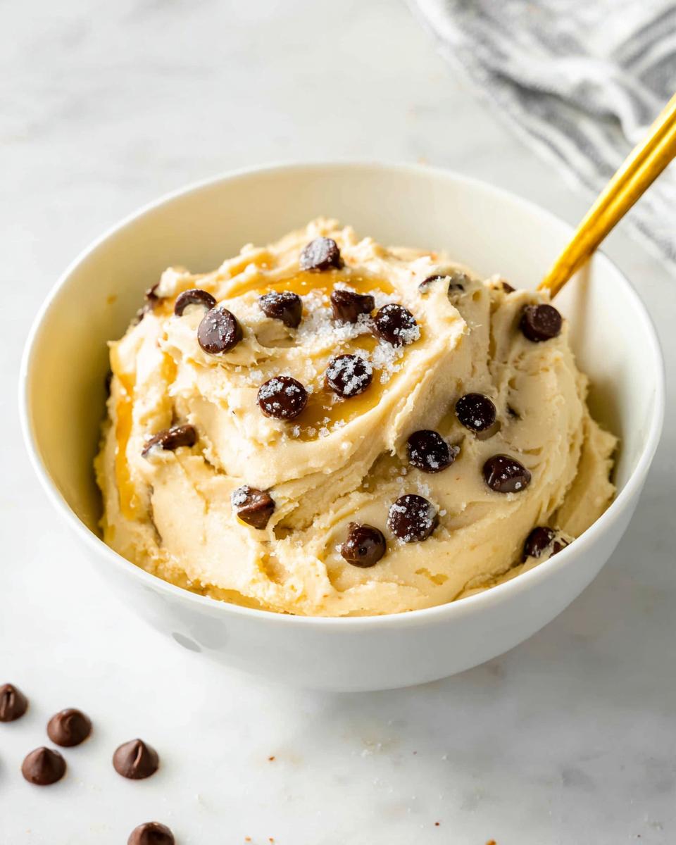 A bowl of creamy Greek Yogurt Cookie Dough topped with chocolate chips and sea salt, ready to be eaten with a spoon.