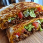 A close-up of a homemade ground beef crunchwrap, cut in half, showing seasoned ground beef, melted cheese, lettuce, and tomatoes.