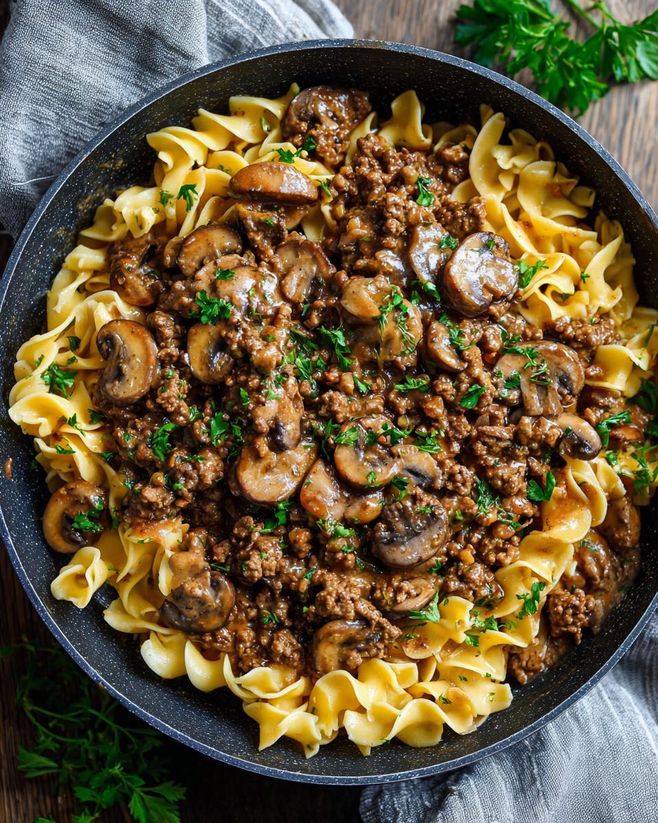 A close-up overhead view of a creamy ground beef stroganoff skillet meal with egg noodles and mushrooms, garnished with parsley.