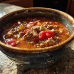 A close-up of a rustic bowl filled with comforting hamburger soup, featuring ground beef, tomatoes, and vegetables.