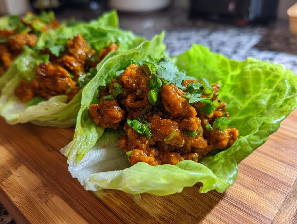 Close-up of two fresh chicken lettuce wraps, filled with seasoned chicken and topped with green onions and cilantro.