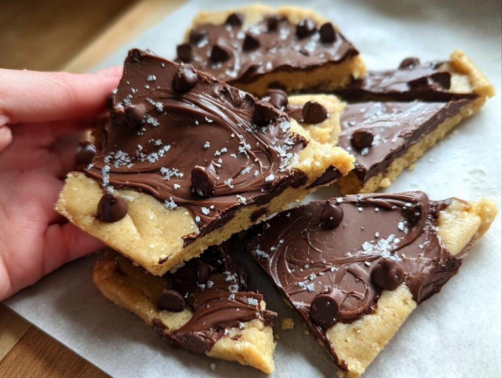 A hand holding a piece of Healthy Cookie Dough Bark topped with chocolate chips and sea salt.