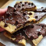A hand holding a piece of Healthy Cookie Dough Bark topped with chocolate chips and sea salt.