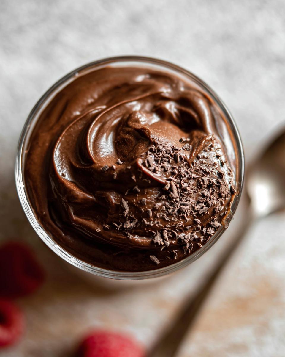 A close-up overhead view of a glass filled with rich, swirled High Protein Chocolate Pudding, topped with chocolate shavings.