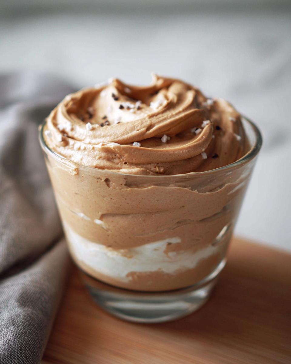 A close-up of a glass filled with creamy High-Protein Cottage Cheese Peanut Butter Mousse, topped with a sprinkle of sea salt and chocolate shavings.