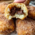 A close-up of a homemade churro bite, split open to reveal a gooey Nutella filling, coated in cinnamon sugar.