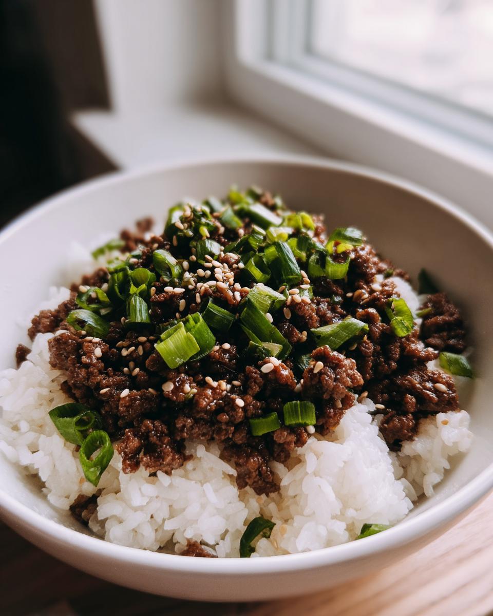 A close-up of a Korean beef rice bowl, featuring seasoned ground beef over white rice, topped with chopped green onions and sesame seeds.
