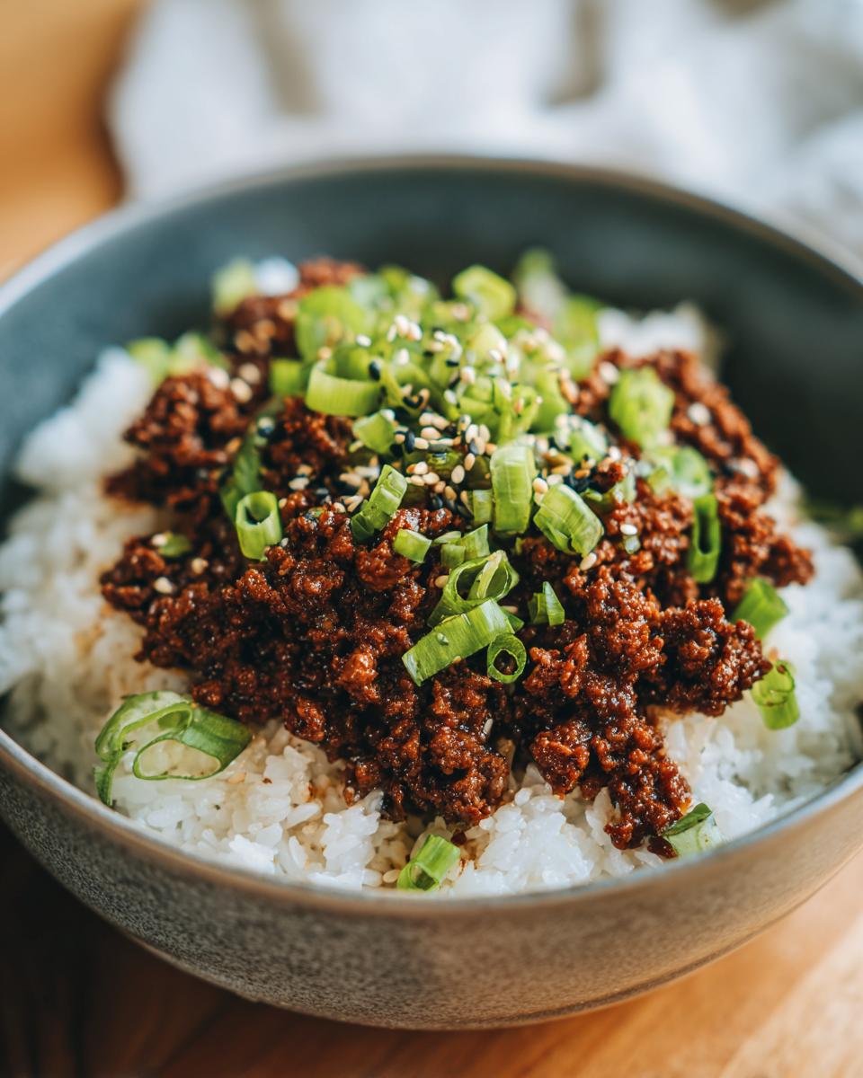 A close-up of a Korean beef rice bowl topped with seasoned ground beef, chopped green onions, and sesame seeds.