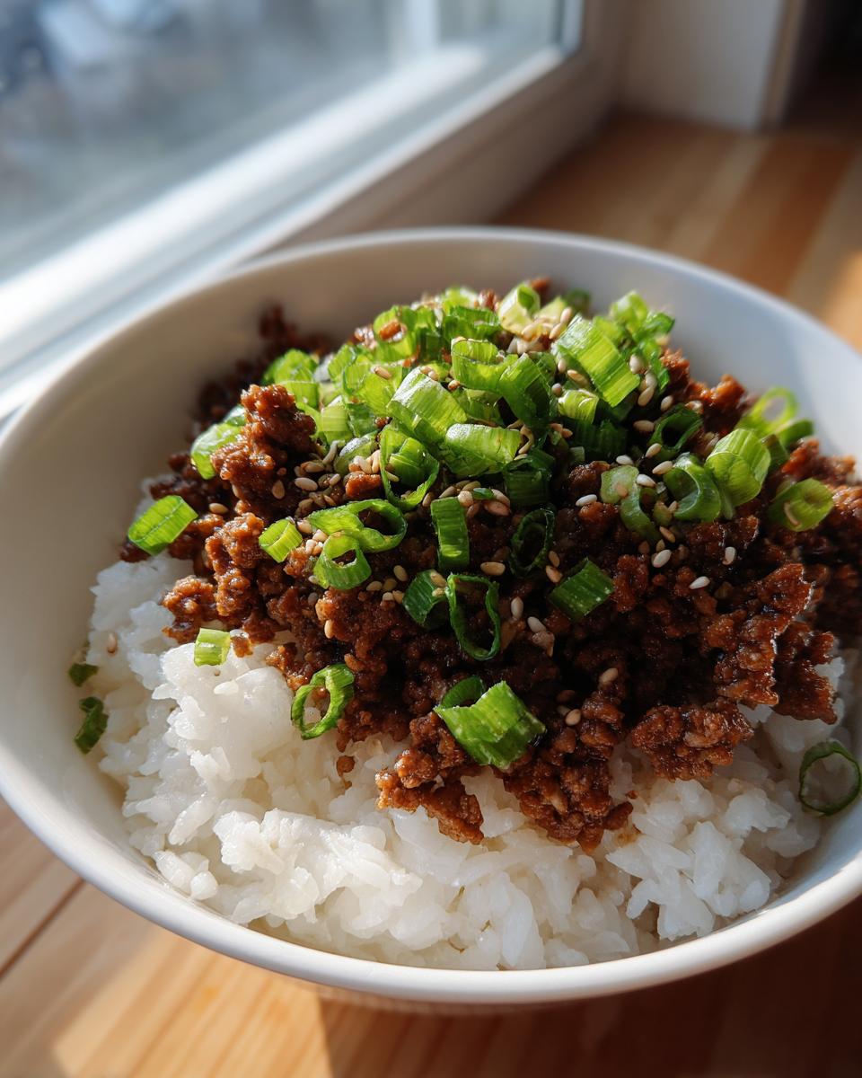 A close-up of Korean beef rice bowls with ground beef, topped with chopped green onions and sesame seeds.