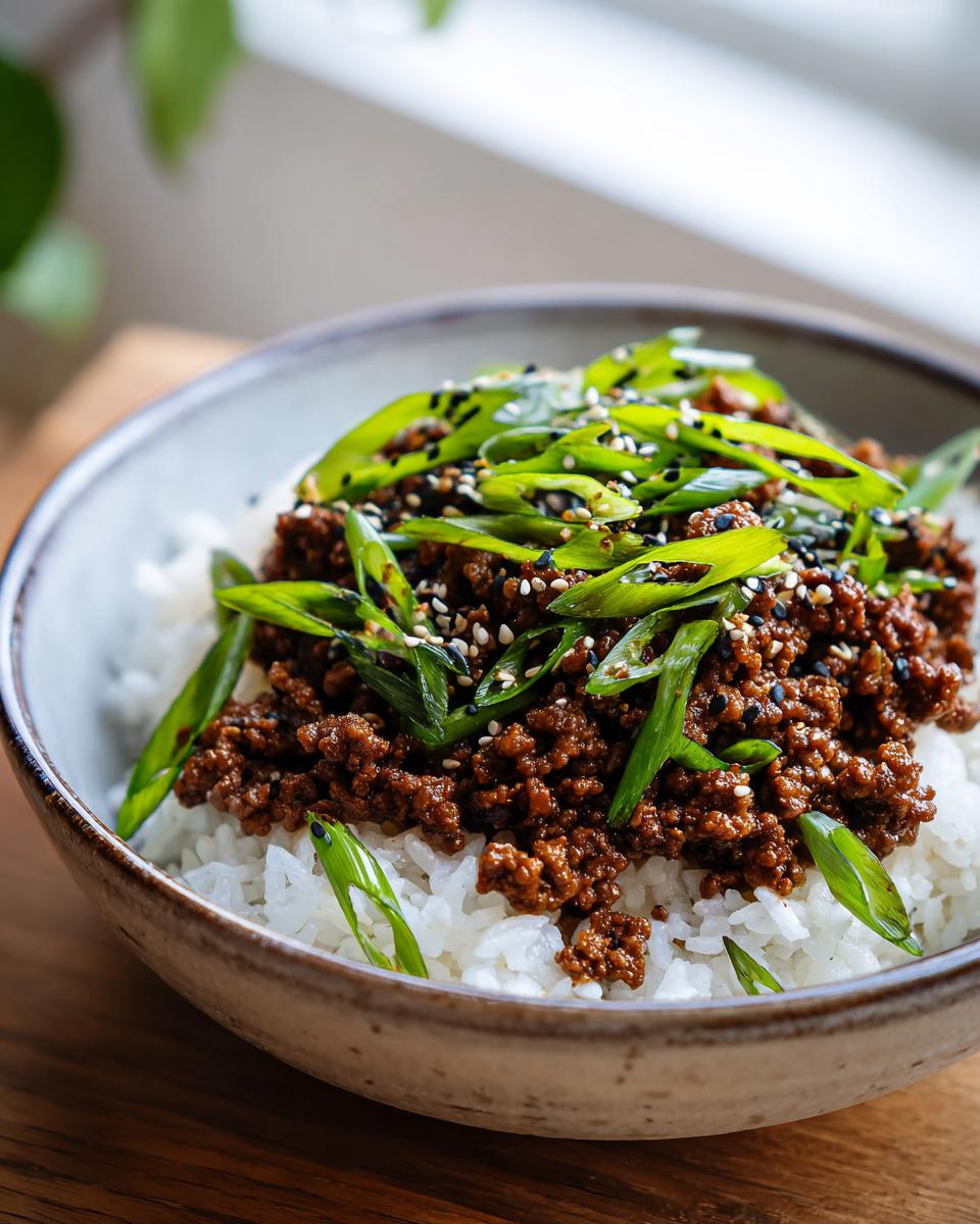 A close-up of a Korean ground beef rice bowl topped with green onions and sesame seeds.