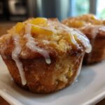 Close-up of two moist peach muffins topped with a sweet vanilla glaze.