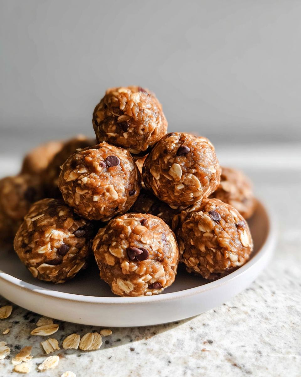 A close-up stack of no-bake chocolate peanut butter protein balls on a white plate, showing oats and chocolate chips.