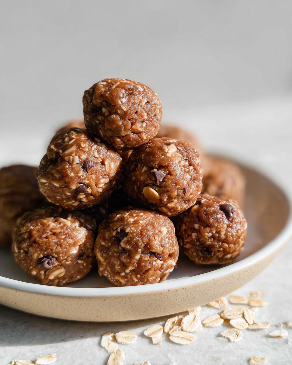 A close-up stack of No-Bake Chocolate Peanut Butter Protein Balls on a plate with scattered oats.