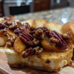 Close-up of baked brie topped with peaches, toasted pecans, and a glaze, served with toasted baguette slices.