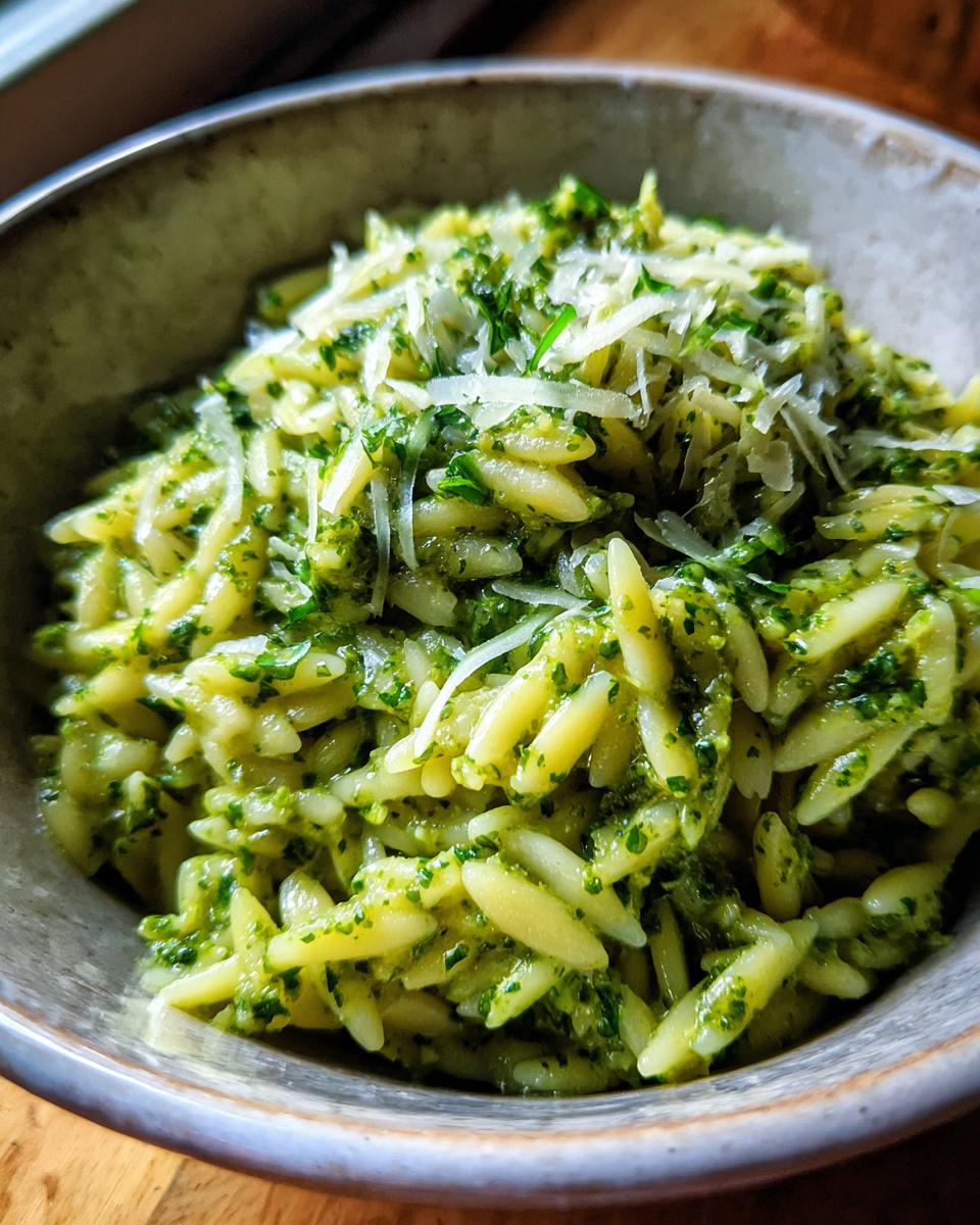 A close-up of a bowl filled with bright green pesto orzo pasta, topped with grated Parmesan cheese.