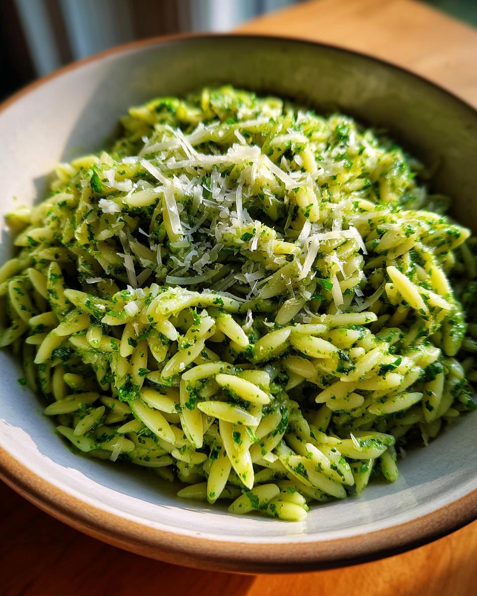A close-up of a bowl of bright green Pesto Orzo pasta, topped with grated Parmesan cheese.